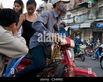 Un chauffeur de taxi moto prend de deux femmes passagers près d'un marché très fréquenté sur une rue de ville de Phnom Penh, Cambodge. Banque D'Images