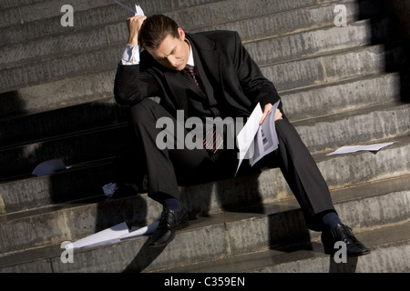 Photo de l'homme triste avec des papiers dans les mains assis sur des escaliers avec aucune idée de quoi faire Banque D'Images