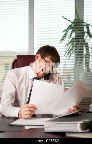 Photo de patron émotionnelle en criant récepteur du téléphone tout en regardant à travers des articles dans office Banque D'Images