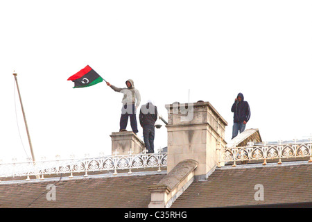 Les manifestants d'avoir accès au toit de l'ambassade de Libye à Londres et se déployer le drapeau rouge et noir vert Banque D'Images