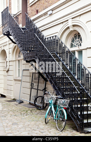 Bicyclette verte enchaîné à un noir, escalier en fer forgé dans une étroite ruelle pavée à Windsor, Berkshire, England, UK Banque D'Images