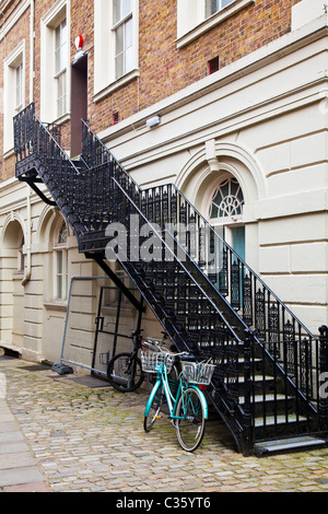 Bicyclette verte enchaîné à un noir, escalier en fer forgé dans une étroite ruelle pavée à Windsor, Berkshire, England, UK Banque D'Images