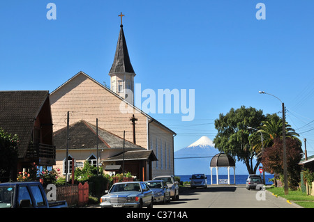 Voitures garées dans une rue par des bardeaux de bois Eglise luthérienne, en regardant vers le Lac Llanquihue et le volcan Osorno, Frutillar, Chili Banque D'Images