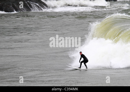 Lone surfer sur Washington's rocky coast surf avec cliffs clairement en arrière-plan sur un jour d'avril pluvieux près de Columbia River Banque D'Images