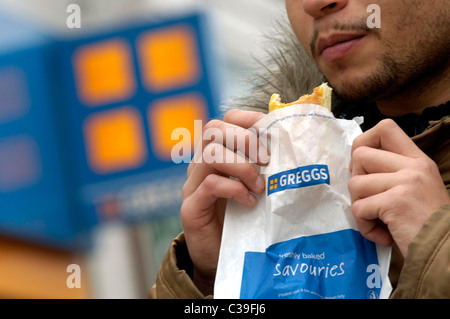 Un homme mange son achat récemment Greggs la nourriture. Banque D'Images