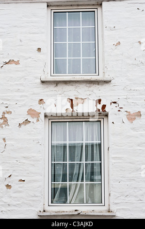 Deux fenêtres dans un mur peint en blanc. La peinture s'écaille et en décomposition le mur du fait de l'exposition à la station météo. Banque D'Images