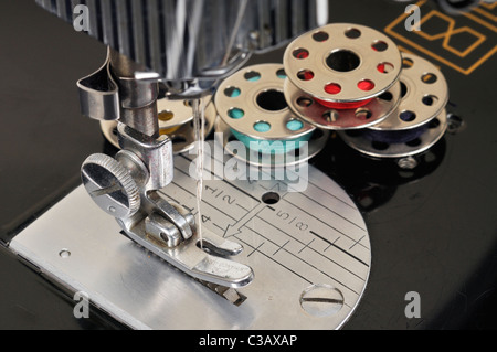 Aiguille filetée et bobines de fil d'attente avec une ancienne machine à coudre Singer close-up. Banque D'Images