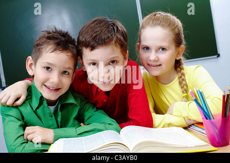 Portrait de deux gars et fille assise en classe avec livre ouvert près de par Banque D'Images