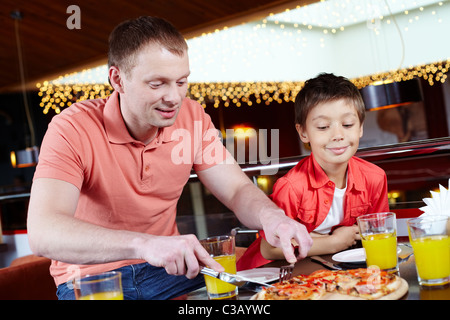 Portrait of handsome man cutting pizza avec son fils dans une pizzeria à proximité Banque D'Images