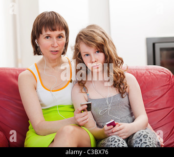 Mère et fille adolescente assise sur canapé ensemble et à l'écoute de lecteurs mp3 Banque D'Images