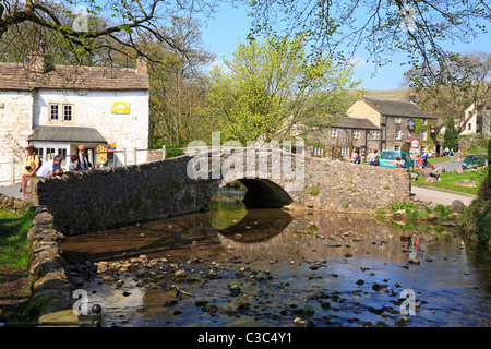 Les promeneurs sur le pont de pierre sur Malham Beck à Malham, Malhamdale, Yorkshire du Nord, Yorkshire Dales National Park, England, UK. Banque D'Images