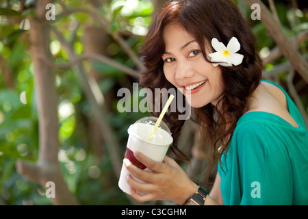 Smiling asian femme thaïlandaise de boire du jus de fruits avec une fleur dans les cheveux Banque D'Images