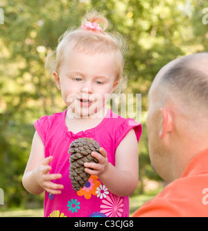 Adorable jeune Girl Holding Pine Cone parle à son père dans le parc. Banque D'Images