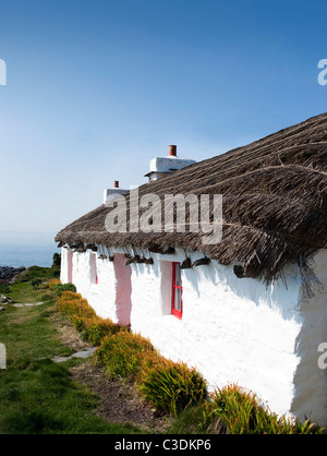 Ancienne maison au toit de chaume blanc et fenêtres rouges sur fond de ciel bleu au bord de la mer Banque D'Images