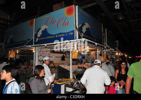 Foule de clients autour d'un étal avec 2 hommes en blouse blanche la vente de poissons frais et de fruits, Mercado Central, Santiago, Chili Banque D'Images