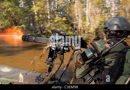 Membre de l'équipe de l'US Navy SEAL prévoit couvrir le feu avec un minigun lors d'une plage de la rivière étroite de la pratique de l'extraction. Banque D'Images