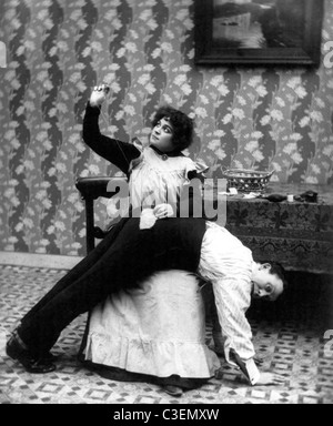 Un point à temps enregistre neuf - homme penché au-dessus de genoux de femme comme elle coud patch sur son pantalon' siège, vers 1907. Banque D'Images