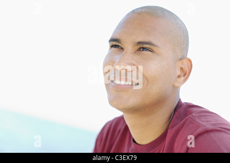 Portrait of young hispanic guy avec tête rasée à la recherche vers le ciel près de la mer. Banque D'Images