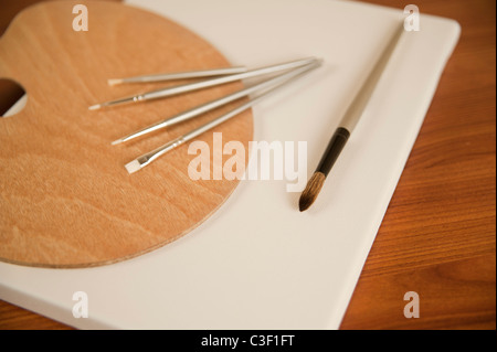 Un ensemble de nouvelles brosses et une palette en bois sont placés au sommet d'une toile vierge dans un studio d'art. Banque D'Images