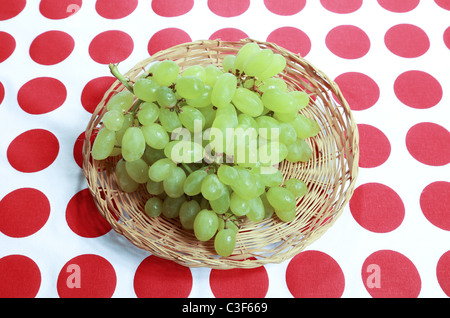 Raisins verts frais dans un plat peu profond de baster en osier sur une nappe avec des points rouges Banque D'Images