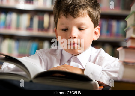 Close-up of cute boy reading book lors de la préparation de la leçon dans la bibliothèque Banque D'Images