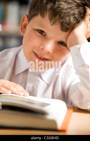 Close-up of smiling schoolkid toucher page de livre ouvert et à la recherche à l'expression positive avec l'appareil photo Banque D'Images