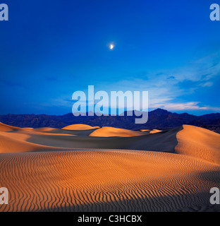 La lumière du soleil tôt le matin fusionne avec un crépuscule lune au-dessus des dunes de sable et des montagnes à Death Valley National Park, California, USA Banque D'Images