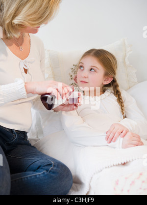 Donner des médicaments à la mère fille (10-11) in bed Banque D'Images