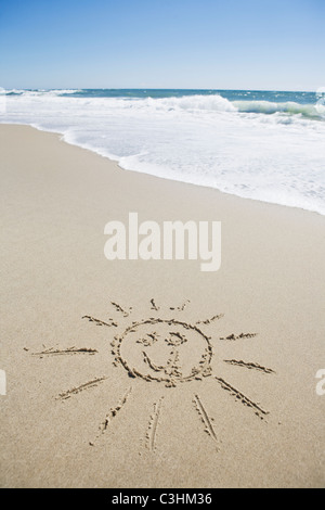 Visage soleil dessiné sur une plage de sable Banque D'Images