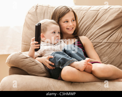 Girl (10-11) avec le frère (2-3) sitting on sofa, watching TV Banque D'Images