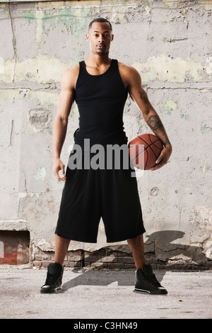 Portrait de jeune homme au basket-ball contre le mur délabré Banque D'Images