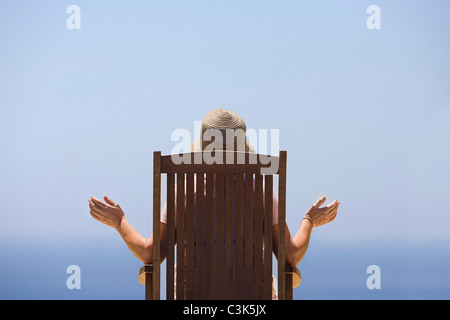 Vue arrière de la femme assis sur chaise en bois, face à la mer Banque D'Images