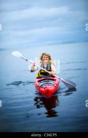 Woman rowing canoe on lake, smiling Banque D'Images