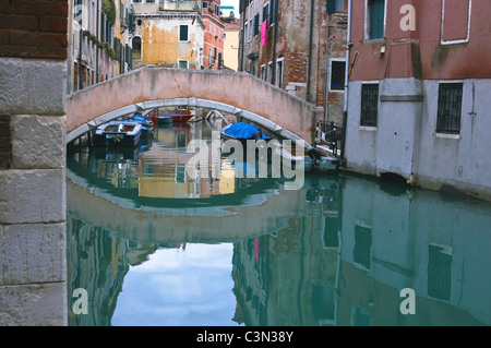 Dans un bras mort à Venise le long d'un canal vers un pont avec des maisons de chaque côté et la scène qui se reflète dans l'eau. Banque D'Images