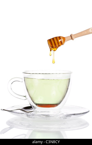 Gouttes de miel d'un balancier de miel en verre tasse à thé vert sur fond blanc Banque D'Images