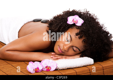 Femme heureuse à santé Day spa avec massage aux pierres chaudes en serviette blanche sur table en bambou décoré d'orchidées. Banque D'Images