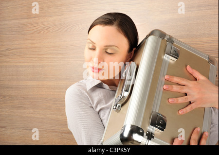 Portrait d'une belle jeune businesswoman holding a suitcase amoureusement. Arrière-plan de bureau. Banque D'Images