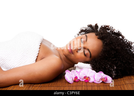 Femme brésilienne à un spa de jour, portant sur bambou table de massage avec la tête sur l'oreiller portant une serviette et fleurs orchidée autour. Banque D'Images