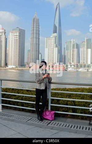 Parution modèle femme chinoise à l'aide d'iPhone avec des gratte-ciel de Pudong dont le World Financial Center à l'arrière-plan Banque D'Images