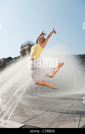 Allemagne, Munich, Karlsplatz, jeune femme sautant en l'air Banque D'Images