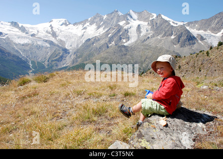 Un jeune garçon est assis de déguster une boisson et un pique-nique à Kreuzboden dans la vallée de Saas, la Suisse. Banque D'Images