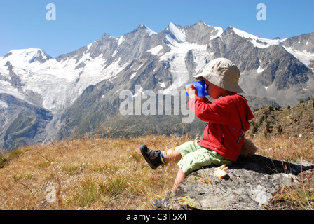 Un jeune garçon est assis de déguster une boisson et un pique-nique à Kreuzboden dans la vallée de Saas, la Suisse. Banque D'Images