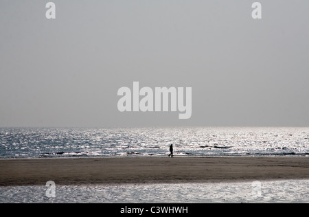 La silhouette d'une figure marchant sur un Cornish déserte plage à marée basse Banque D'Images