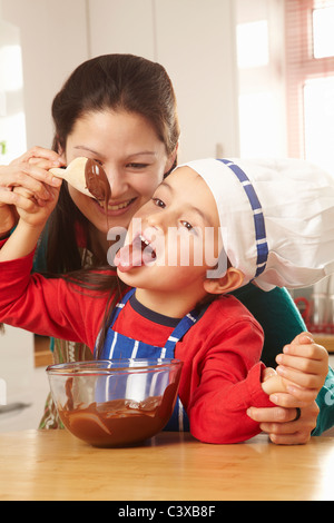 Boy licking chocolat de spoon avec maman Banque D'Images