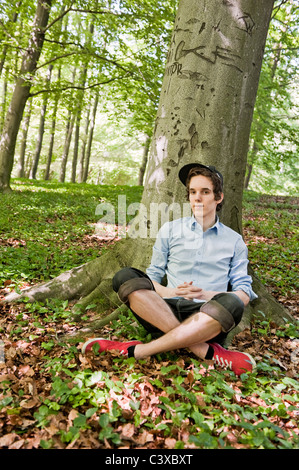 Jeune homme assis en face d'un arbre dans les bois Banque D'Images