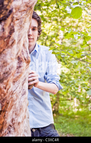 Jeune homme debout par un arbre dans les bois Banque D'Images