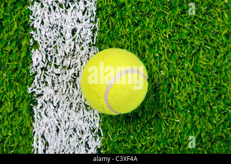 Photo d'une balle de tennis sur gazon d'un côté de la ligne blanche, tourné à partir de ci-dessus.