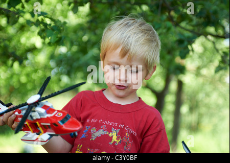 Un Enfant Jeune garçon blond jouer avec un jouet pompier Lego hélicoptère de sauvetage et l'hélicoptère de police à l'extérieur Banque D'Images