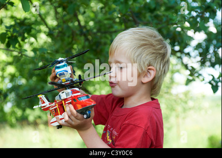 Un Enfant Jeune garçon blond jouer avec un jouet pompier Lego hélicoptère de sauvetage et l'hélicoptère de police à l'extérieur Banque D'Images