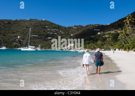 Scène romantique de l'homme et de la femme tenant la main marchant le long d'une jolie plage avec des maisons sur la colline et voiliers dans l'eau Banque D'Images